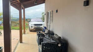 Un espace extérieur abrité, avec une voiture blanche garée à l’extérieur, un canapé noir et un sol carrelé.