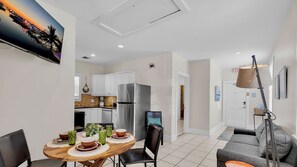 A modern kitchen with white cabinets, a stainless steel refrigerator, and a dining area with a wooden table and chairs.