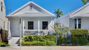 Ein weißes, zweistöckiges Haus mit Veranda, kleinem Garten und schwarzem Zaun.