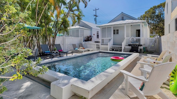 A swimming pool with lounge chairs, a deck, and a white fence.