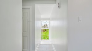 Un passadís amb una porta que condueix a una habitació, una finestra amb vista a un camp verd i una paret blanca.