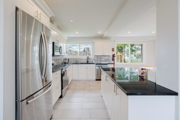 A modern kitchen with white cabinetry, stainless steel appliances, and a black countertop.