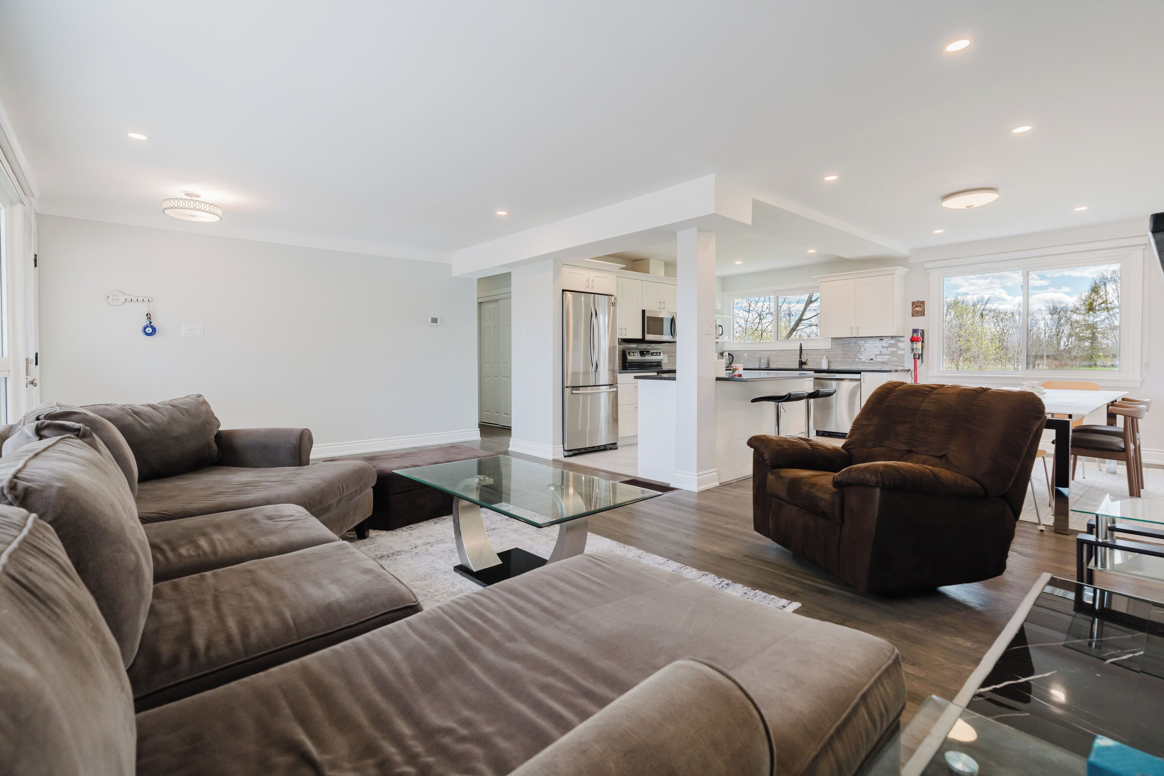 Una sala de estar moderna con un sofá modular, una mesa de centro de vidrio y un sillón marrón.