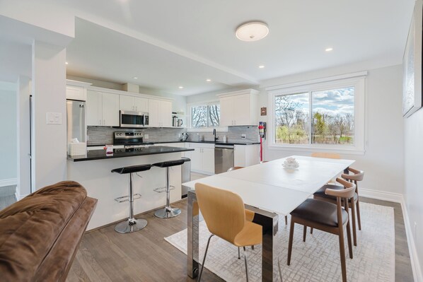 A modern kitchen with white cabinets, stainless steel appliances, and a large window.