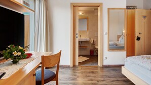 Une chambre à coucher avec un lit, un bureau et une chaise, une fenêtre et une salle de bain visible à travers une porte ouverte.