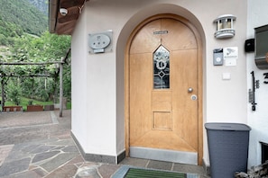 A wooden door with a glass panel, a mailbox, a security camera, and a trash bin. - Apartment "Double Room" with Mountain View, Shared Pool and Wi-Fi (Algund)