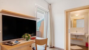 Une chambre équipée d’une télévision, d’un bureau, d’une chaise, d’une fenêtre et d’une salle de bain avec un lavabo et un miroir.
