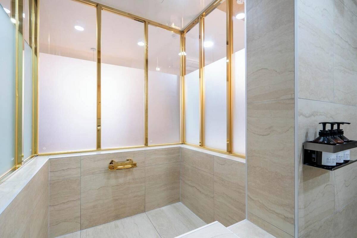 A modern bathroom with a glass enclosure, a gold-framed window, and a marble floor.