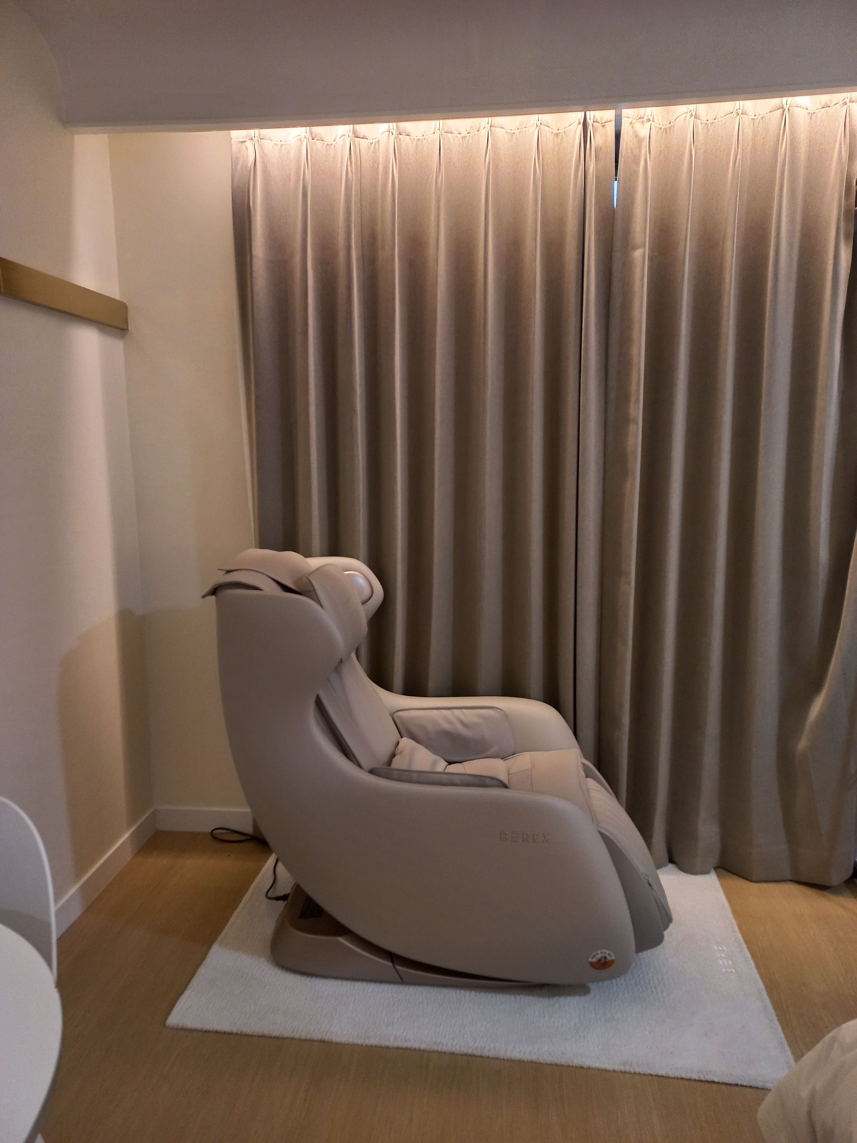 Una silla de masaje en una habitación con una cortina grande y un tapete blanco.