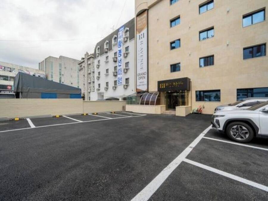 A parking lot with a white car, a building with multiple floors, and a sign that reads 'GRAND OPEN'.