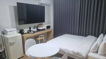 Ein Hotelzimmer mit einem Bett, einem Schreibtisch mit Computer und Telefon, einer kleinen Kühlschrank, einem Fernseher und einem Fenster mit Vorhängen.