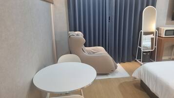 Quarto de hotel com cama, cadeira de massagem, uma pequena mesa, espelho e televisão.
