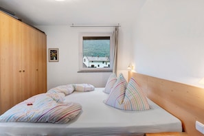 Ein Schlafzimmer mit Bett, Kissen, einem Holzschrank, einem Fenster mit Aussicht und einer Wandleuchte.