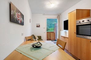 Eine Küche mit Holzausstattung, einem Esstisch mit Stühlen, einem Bild an der Wand und Blick durch die Tür.