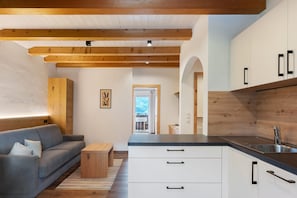 A modern kitchen with wooden beams, a grey sofa, and a view to the outside. - Apartment “A2” with Mountain View, Shared Pool and Wi-Fi (Algund)