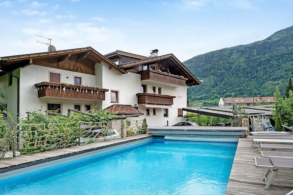 Ein Hotel mit Schwimmbad, Holzterrasse und Bergblick.