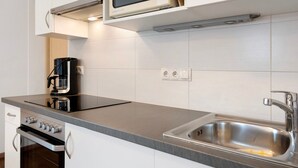 Una cocina moderna con horno integrado, microondas, cafetera y pileta de acero inoxidable.