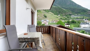 Un balcón con mesa y sillas, con vistas a un paisaje montañoso con viñedos.