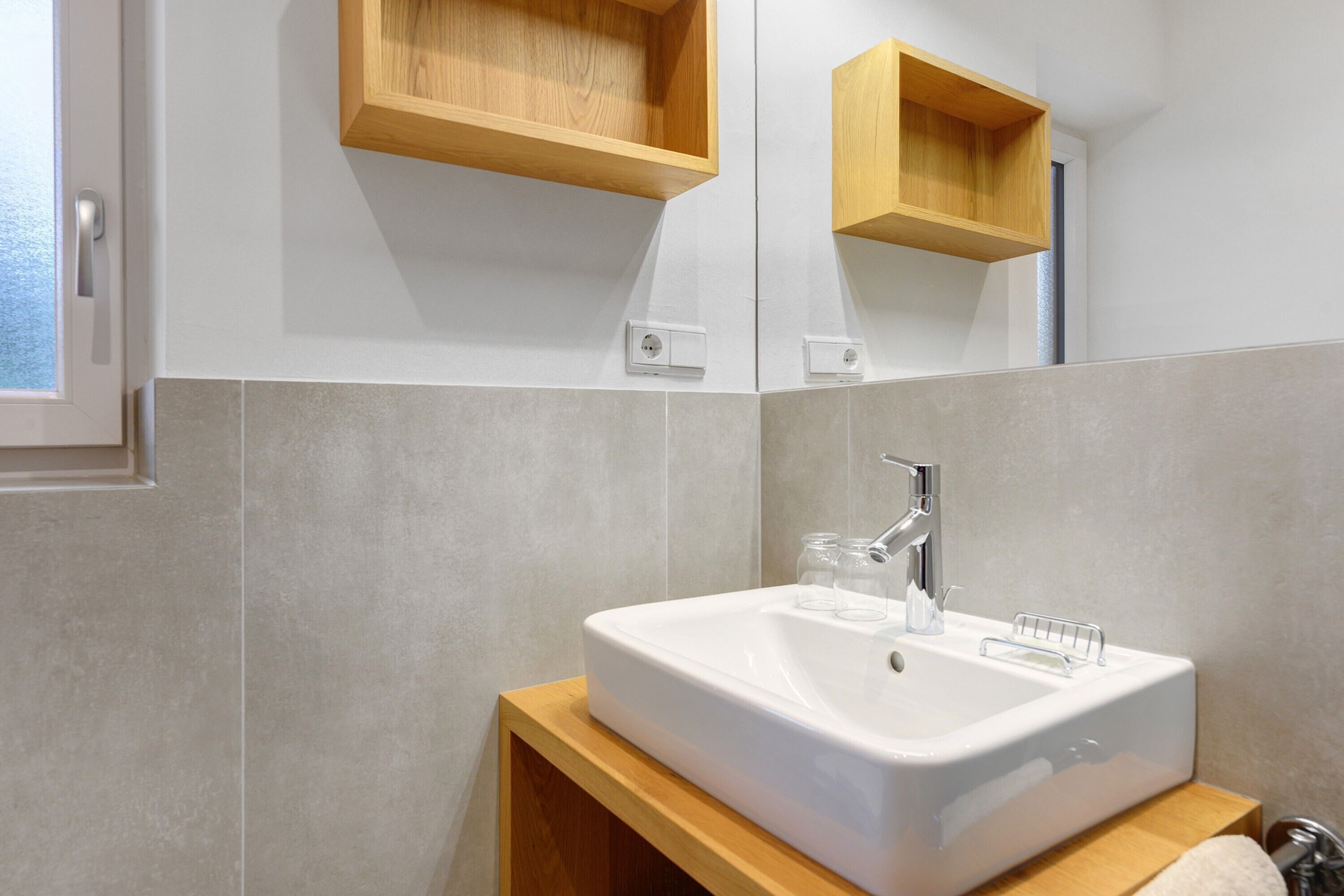 Un bany amb un lavabo blanc, prestatges de fusta i un mirall.