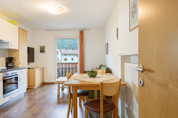 Une cuisine avec des meubles en bois, une table à manger avec des chaises, une fenêtre donnant sur des immeubles et une porte avec une poignée.