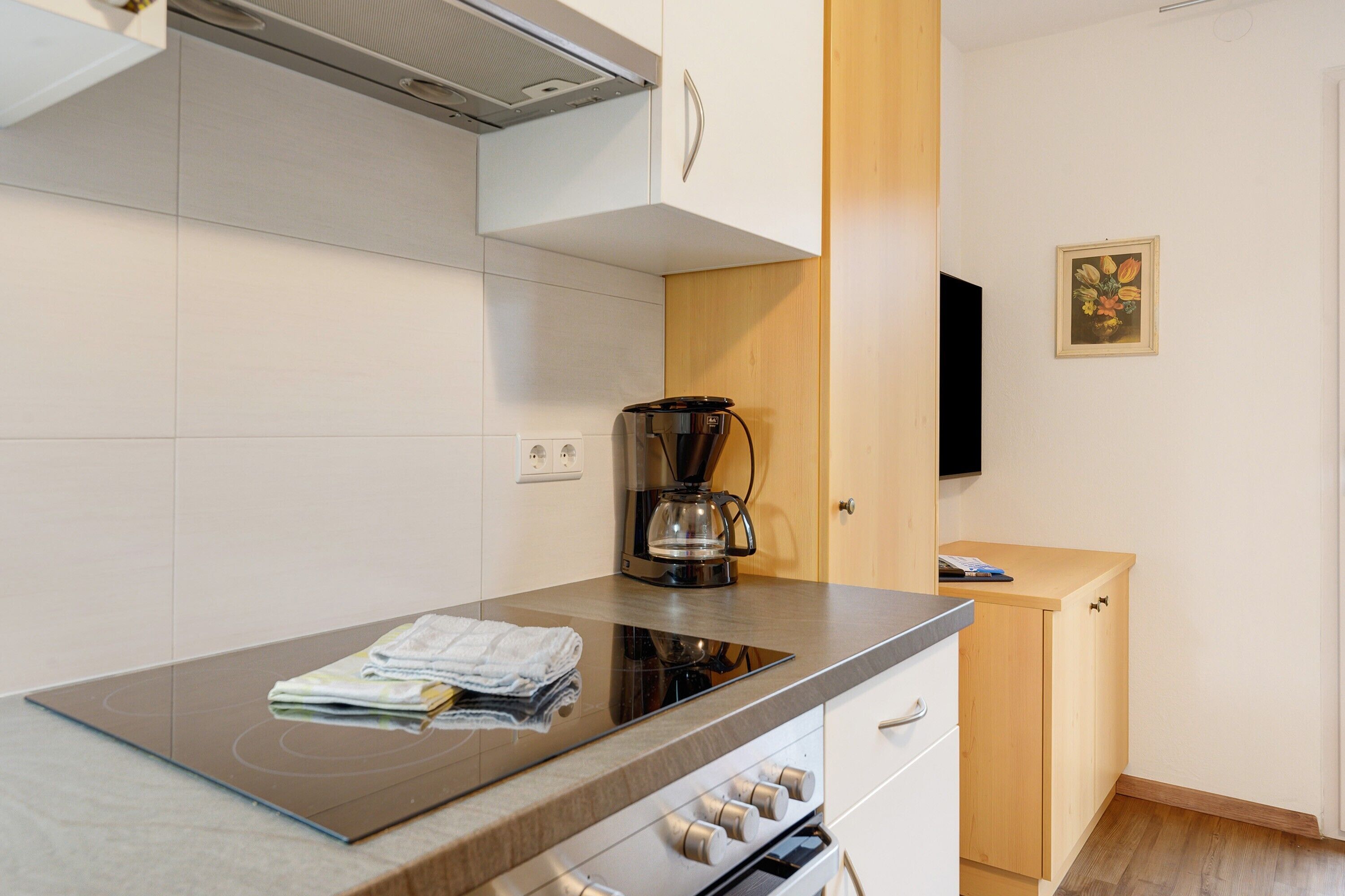 Une cuisine moderne dotée d’une plaque de cuisson à induction intégrée, d’une machine à café et de meubles de rangement en bois.