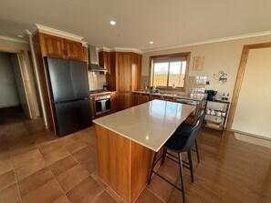 Une cuisine avec des meubles de rangement en bois, un réfrigérateur noir, une cuisinière et un grand îlot central doté de tabourets de bar.