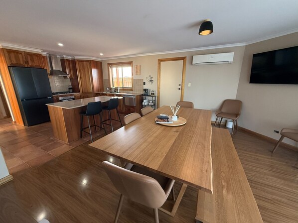 A modern kitchen with wooden cabinets, a black refrigerator, and a dining area with a wooden table and chairs.