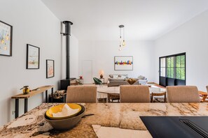 Un salon moderne avec une cheminĂ©e, un coin repas dotĂ© dâune table en marbre et une grande fenĂȘtre.