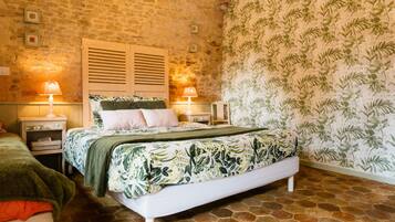 Quarto com parede de pedra, cama com colcha florida, duas luminárias de cabeceira e papel de parede estampado.