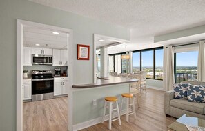 A modern kitchen with white cabinets, a stainless steel oven, and a bar area with stools. - New for 2026 - Beautiful 2 BR 2 BA Unit with Indoor Pool for Year Round Fun! (Ocean City)