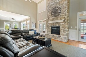 A spacious living room with a stone fireplace, leather sofas, and a large window. - 27523 Medallion Ave., The Peninsula ~ (Millsboro)