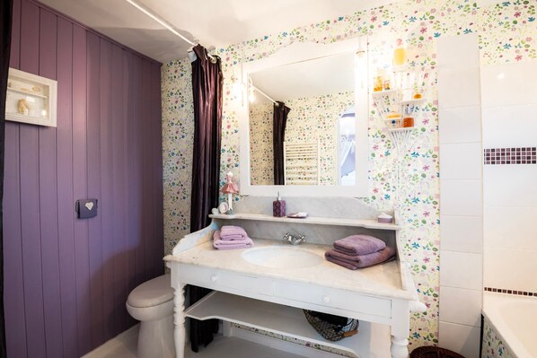 Un baño con una pared morada, un lavamanos blanco, un espejo y una cortina de ducha.