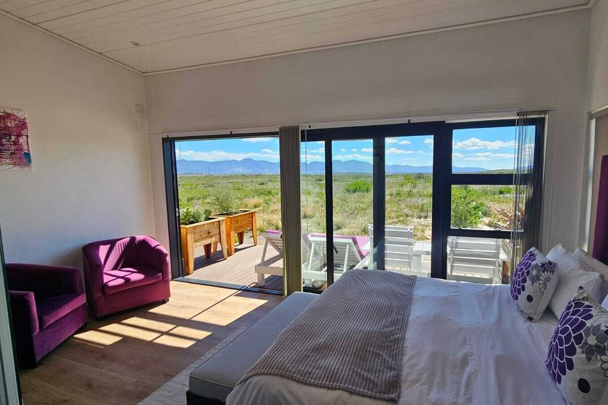 A bedroom with a bed, a purple armchair, and a view of the outdoors.