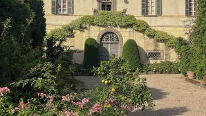 A building with a symmetrical facade, multiple windows with shutters, a central entrance with a decorative arch, and a gravel pathway leading to the entrance. - Villa Rossi Danielli (Lazio)