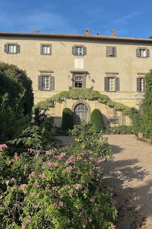 A building with a symmetrical facade, multiple windows with shutters, a central entrance with a decorative arch, and a gravel pathway leading to the entrance. - Villa Rossi Danielli (Lazio)