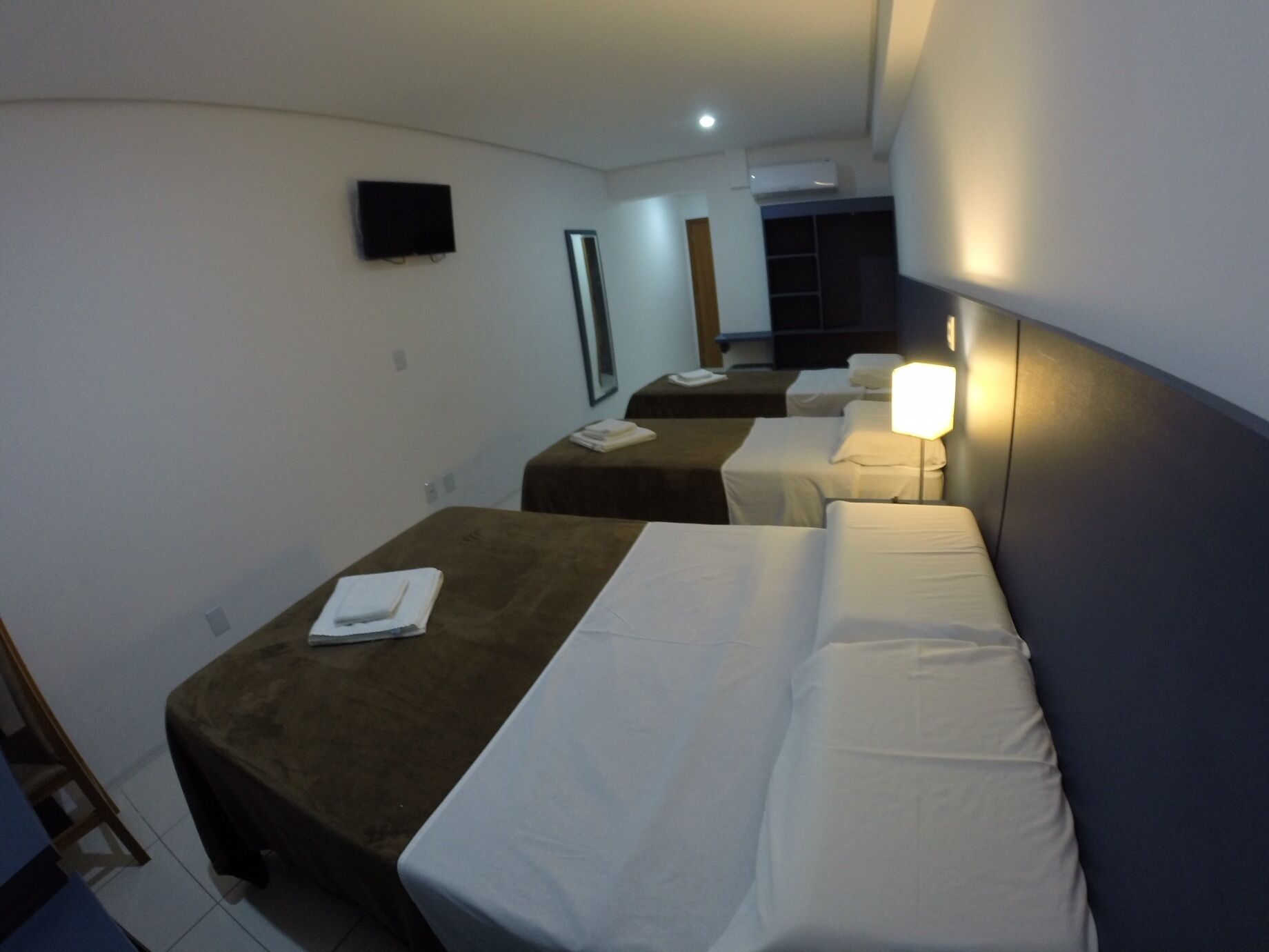 A hotel room with two beds, a TV, an air conditioning unit, and a bedside lamp.
