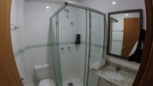 A bathroom with a glass-enclosed shower, a toilet, a sink with a granite countertop, and a mirror.