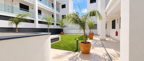 A modern building with multiple balconies, a central courtyard with grass, and potted plants.