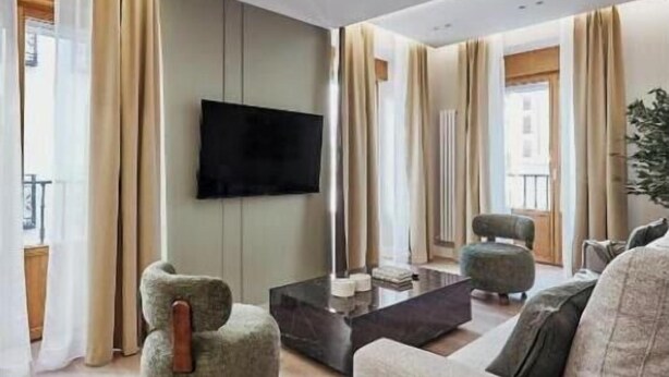 A modern living room with a flat-screen TV, a sofa, a coffee table, and a unique chair. - Spacious Group Apartment in the Heart of Madrid Near Plaza Mayor (Madrid)