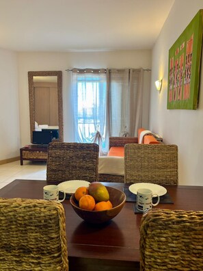 Ein Zimmer mit Esstisch, Korbstühlen, einer Obstschale und einem Bett mit Blick.