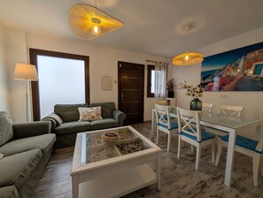 A living room with a sofa, a glass coffee table, a dining table with chairs, and two pendant lights.
