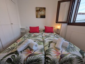 A double bed with floral bedding, two red pillows, and two white towels.