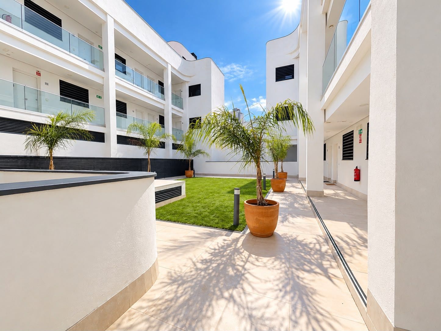 A modern building with multiple balconies, a central courtyard with grass, and potted plants.