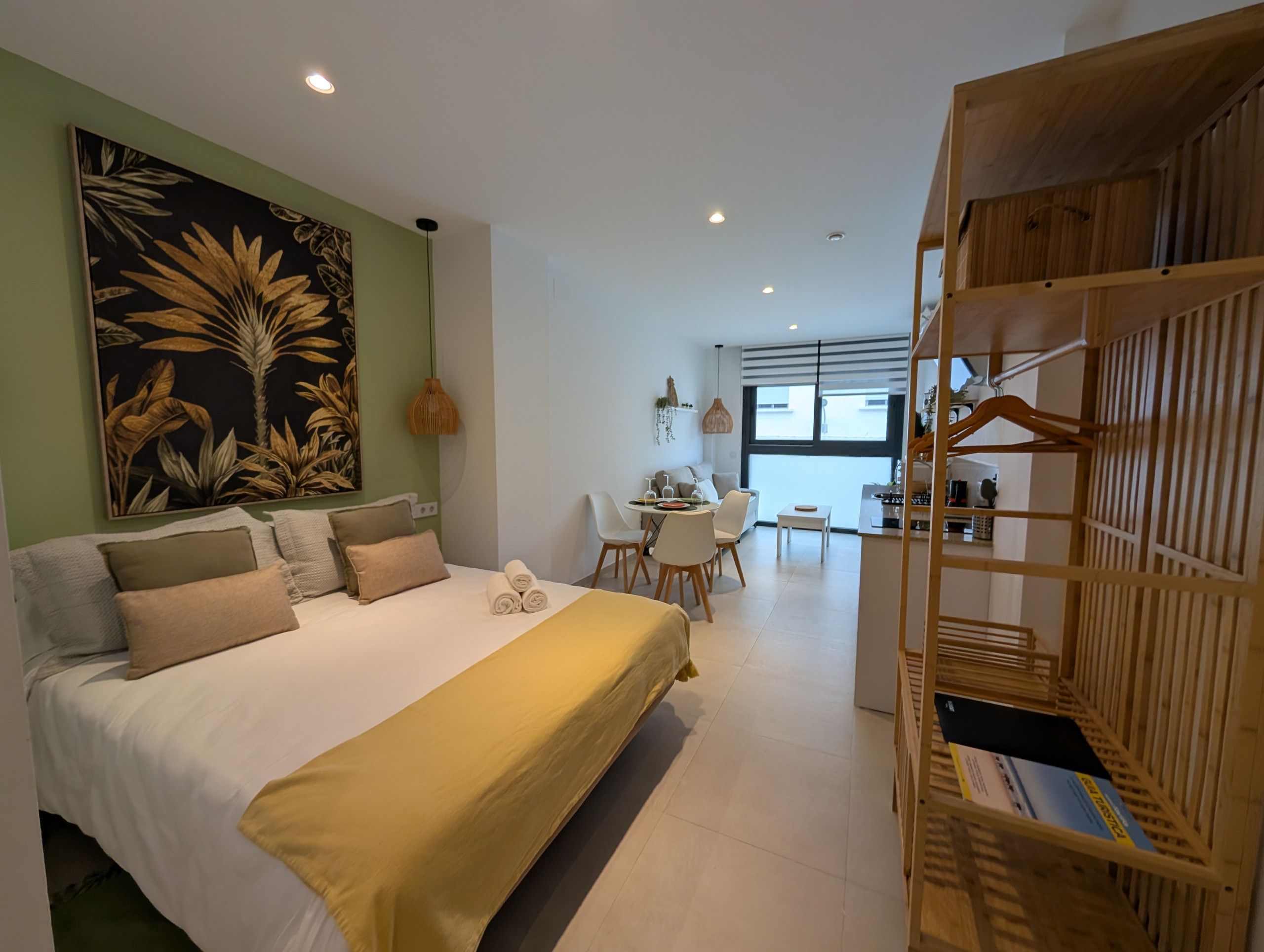 A modern hotel room with a large bed, a dining area, and a wooden wardrobe.