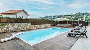A swimming pool with a stone wall and a wooden deck, surrounded by lounge chairs and a covered seating area. - Lara Residence - Agropoli (Agropoli)
