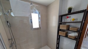 A bathroom with a shower, a window, a shelf with baskets, and a potted plant. - 117 Livingtarifa Trebol (Tarifa)