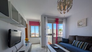 A modern living room with a flat-screen TV, a sofa, a coffee table, and a balcony with a red curtain. - 117 Livingtarifa Trebol (Tarifa)