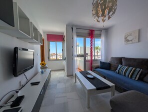A modern living room with a flat-screen TV, a sofa, a coffee table, and a balcony with a red curtain. - 117 Livingtarifa Trebol (Tarifa)