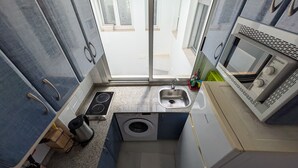 A compact kitchen with a built-in microwave, a sink, a stove, and a washing machine. - 117 Livingtarifa Trebol (Tarifa)
