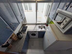 A compact kitchen with a built-in microwave, a sink, a stove, and a washing machine. - 117 Livingtarifa Trebol (Tarifa)